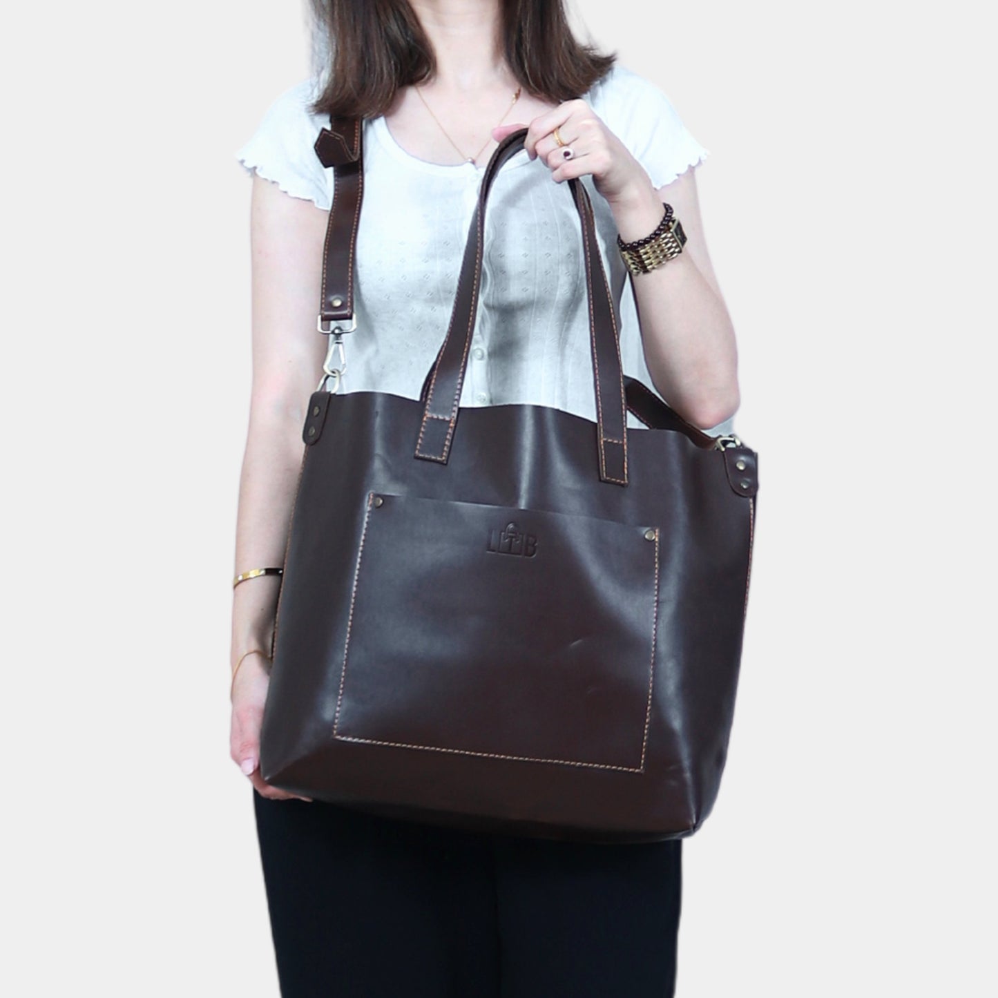 A teenage girl in white shirt holds Ruby Leather Tote with front pocket gracefully in hands