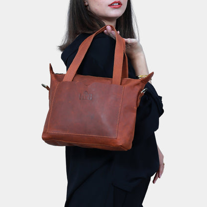 Modern lady in black dress gracefully holding sleek Brown Leather Tote in hands slinging against shoulder