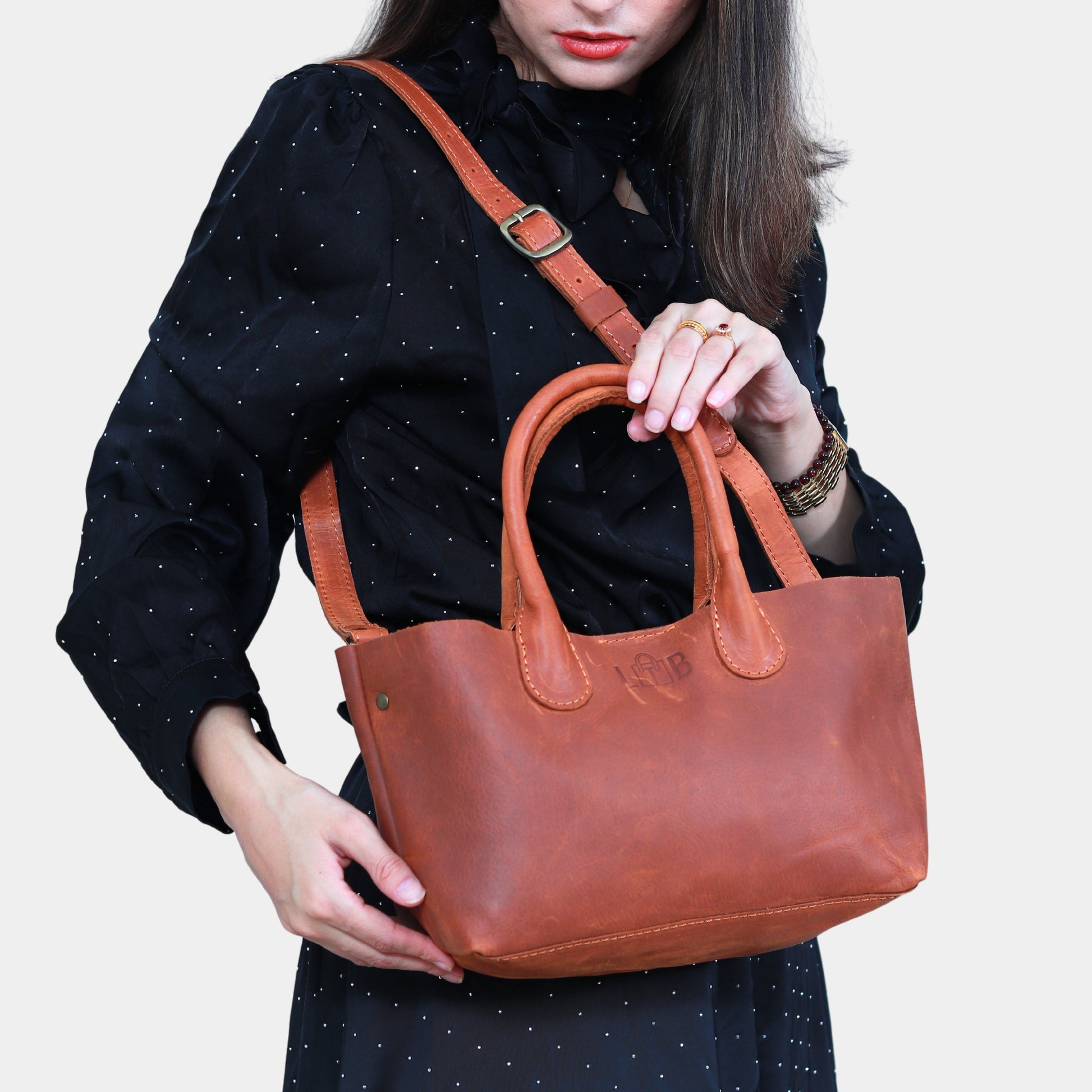 Lady in black dress holding brown small leather tote in hand while slinging it across shoulder 