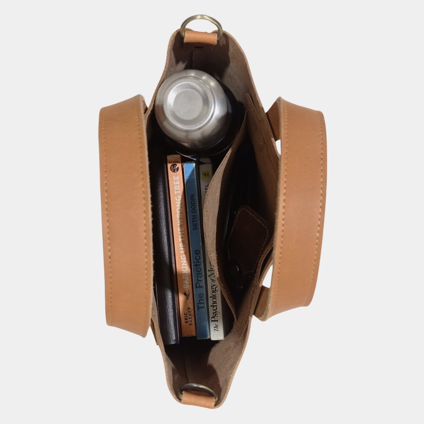 Brown leather Tote with water bottle books and notebooks while keychain and wallet in hanging pocket