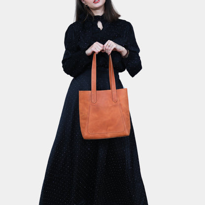 Woman in black dress with small brown leather tote in her hands perfect for weekend outings