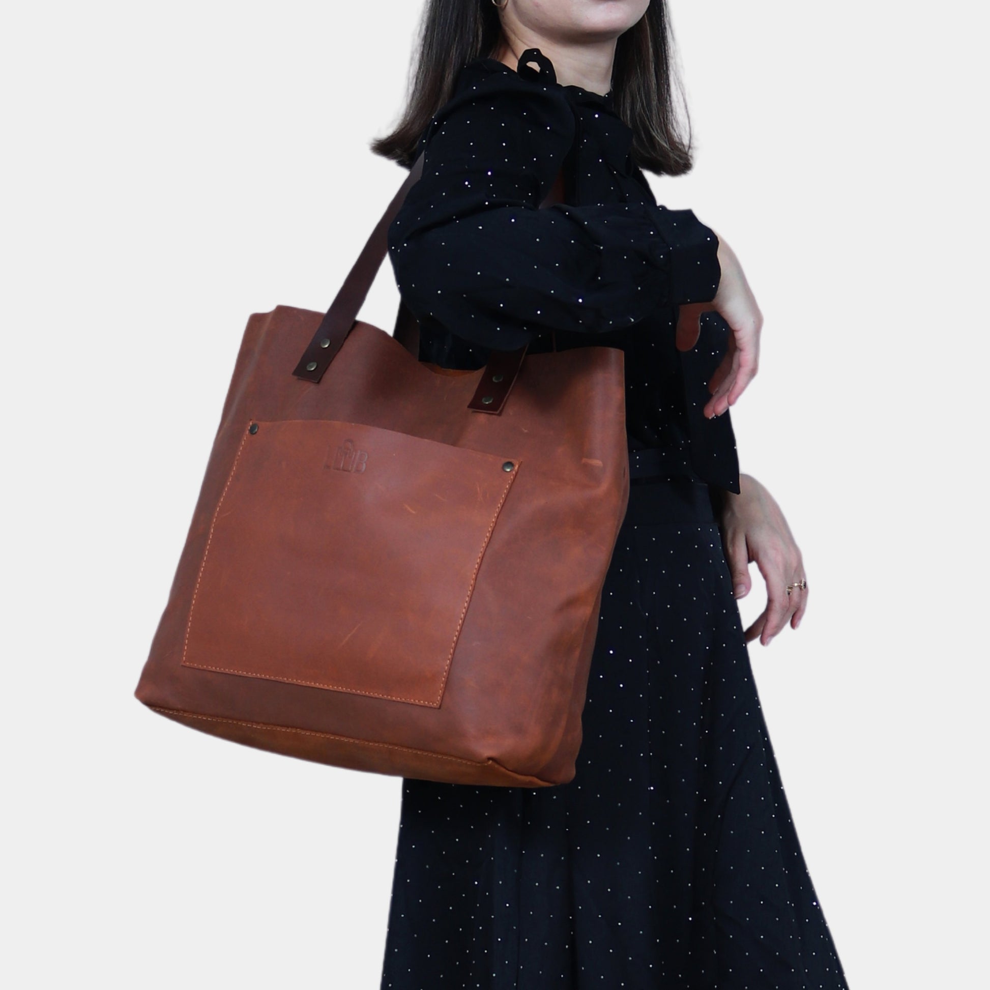 Girl in black dress elegantly slinging Willow Leather Tote with Soft dark brown bridle leather handles